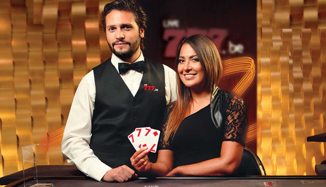 Male dealer in waistcoat and bow tie and female dealer in black dress holding playing cards, against a gold panelled wall.